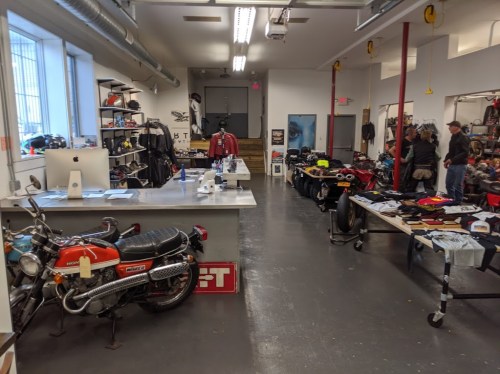 A spacious workshop with vintage motorcycles, apparel, and accessories displayed on tables and shelves.