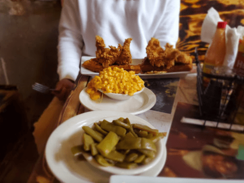 A table with two plates of fried chicken, a bowl of macaroni and cheese, and a plate of green beans.