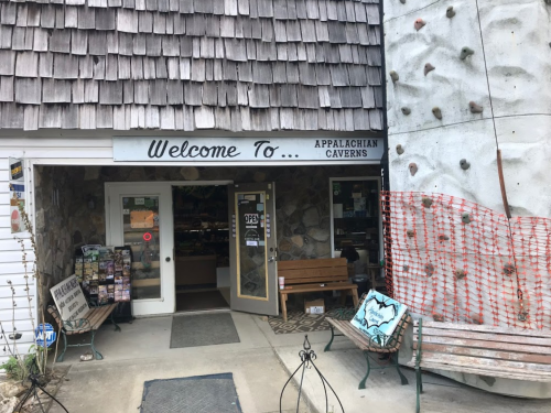 Entrance to Appalachian Caverns with a stone facade, wooden benches, and a rock climbing wall nearby.
