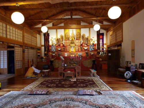 A serene interior of a Buddhist temple featuring a central altar, wooden beams, and decorative rugs.