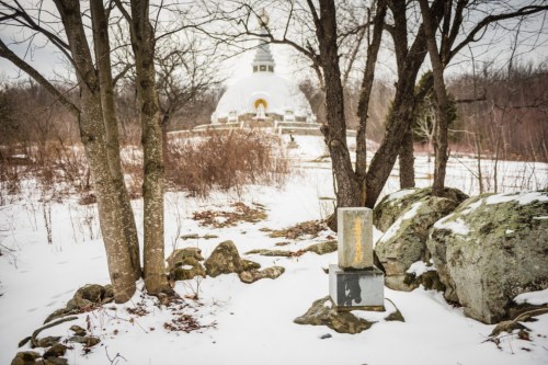 A snowy landscape featuring a stupa in the background, surrounded by trees and rocky terrain.