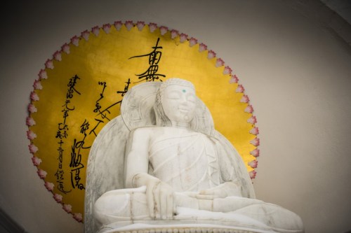 A serene white Buddha statue against a golden circular backdrop with intricate black calligraphy.