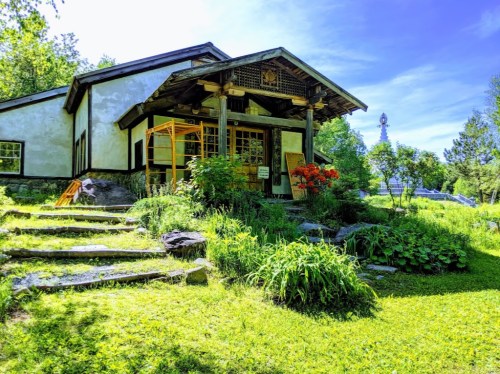 A charming house with a wooden porch, surrounded by lush greenery and colorful flowers under a clear blue sky.