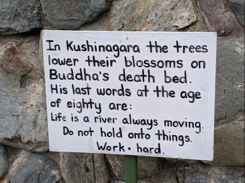Sign on a stone wall with text about Buddha's last words and a reflection on life and hard work.