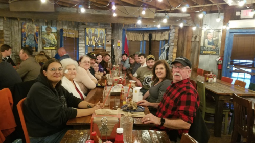 A large group of people gathered around a long table in a rustic restaurant, smiling and enjoying their time together.