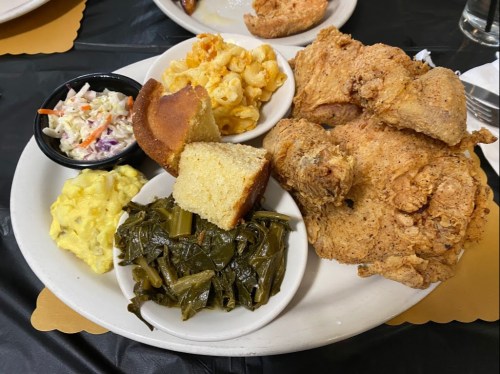 A plate of fried chicken with sides of macaroni and cheese, coleslaw, cornbread, and collard greens.