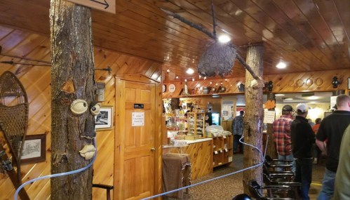 Interior of a rustic restaurant with wooden decor, a unique tree face, and patrons waiting in line.