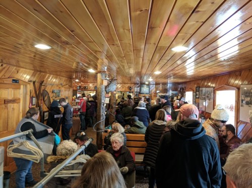 A crowded wooden interior of a restaurant with people waiting in line and sitting on benches.
