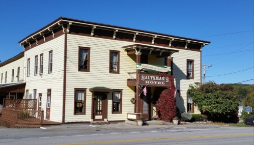 Historic Saltsman's Hotel with a yellow exterior and green accents, surrounded by trees and a clear blue sky.