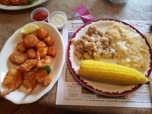 A plate of fried shrimp with a lemon wedge, alongside a dish of corn, stuffing, and creamy side dishes.