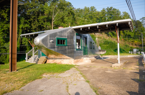 A unique building shaped like a boat, with a metallic exterior and green accents, set in a grassy area.