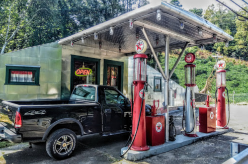 A vintage gas station with a black pickup truck parked at two red gas pumps, featuring an "Open" sign.
