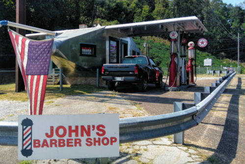 A vintage barber shop resembling a gas station, featuring a truck parked at retro fuel pumps and an American flag.