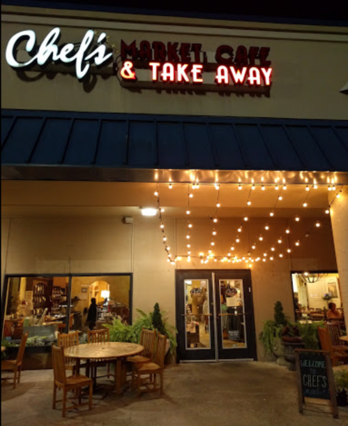 Exterior of Chef's Market Cafe with string lights, wooden tables, and a welcoming sign at night.
