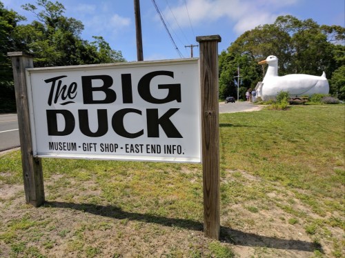 Sign for "The Big Duck" museum and gift shop, featuring a large white duck statue nearby.