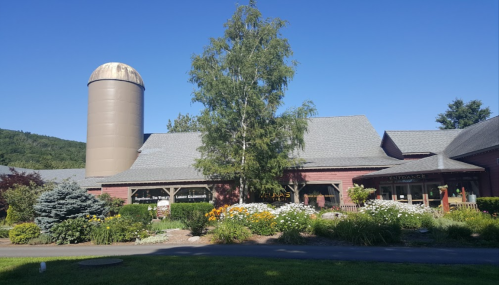 A brick building with a silo, surrounded by colorful flowers and greenery, under a clear blue sky.