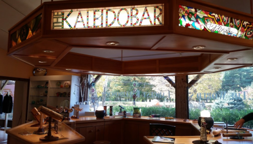 Interior of a shop called "The Kaleidobar," featuring stained glass signage and a view of greenery outside.