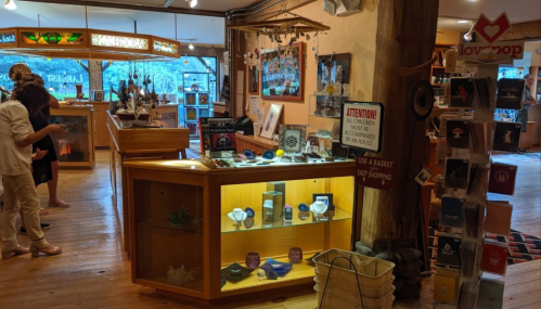 A cozy shop interior with wooden displays, jewelry, and customers browsing among various crafts and decor items.