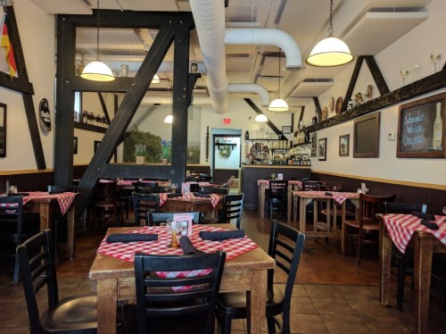 Cozy restaurant interior with wooden tables, checkered tablecloths, and rustic decor. Empty dining area.