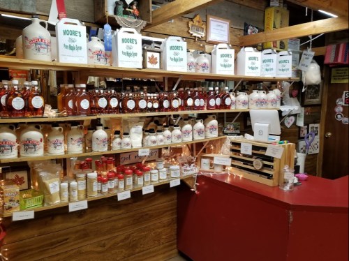 A rustic store display featuring bottles of maple syrup, spices, and various products on wooden shelves.