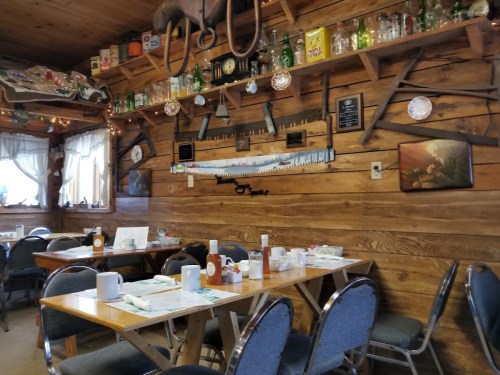 Cozy restaurant interior with wooden walls, tables set for dining, and vintage decor including bottles and tools.
