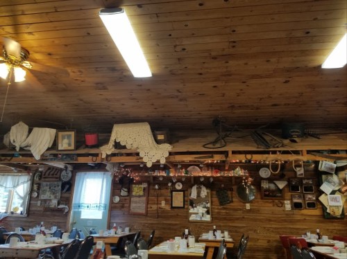 Cozy restaurant interior with wooden walls, vintage decor, and tables set for dining under warm lighting.