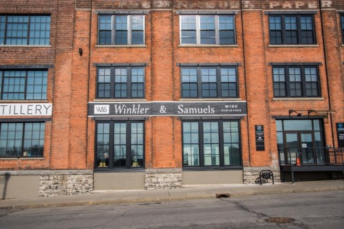Exterior of a brick building featuring a sign for "Winkler & Samuels Wine" with large windows.