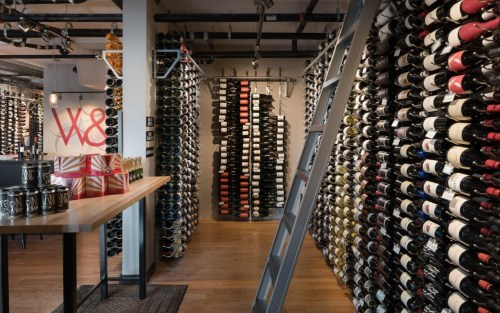 A wine cellar with rows of bottles on the walls and a wooden table with drinks in the foreground.