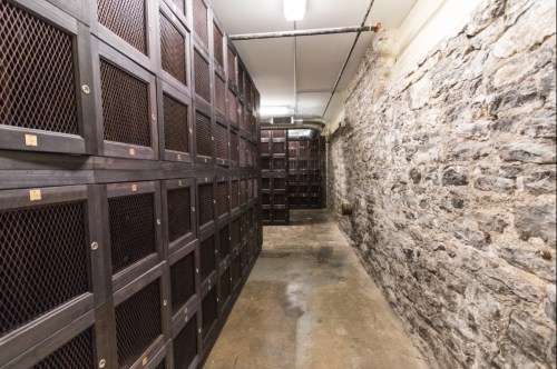 A dimly lit corridor with wooden lockers on one side and a stone wall on the other, creating a rustic atmosphere.