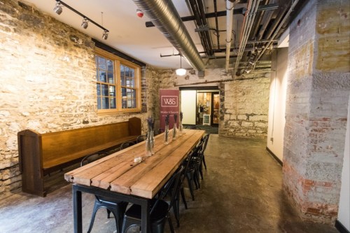 A rustic dining area with a long wooden table, black chairs, and exposed brick walls, featuring a welcoming entrance.
