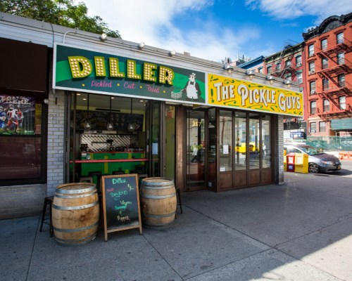 A storefront featuring "Diller" and "The Pickle Guys," with barrels outside and a vibrant, colorful sign.
