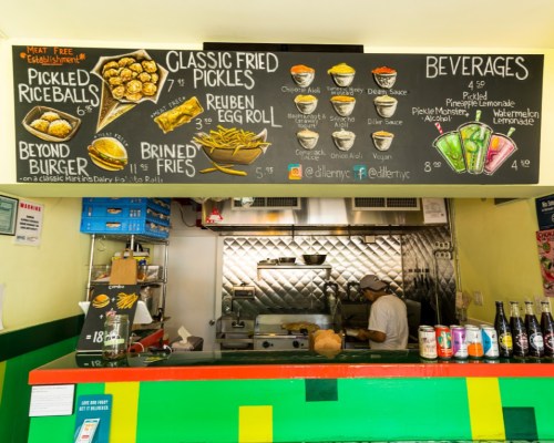 Menu board featuring various food items like fried pickles, rice balls, and burgers, with a chef in the background.