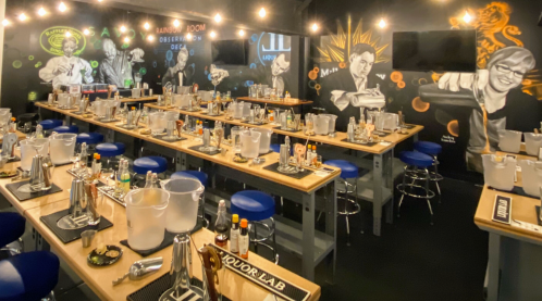 A bar setup with tables, cocktail shakers, and colorful murals on the walls, creating a vibrant atmosphere.