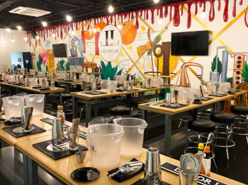 A vibrant bar setup with tables, cocktail equipment, and a colorful mural in the background at Liquor Lab.