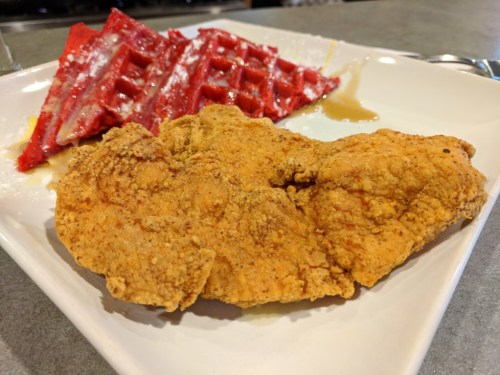 A plate featuring crispy fried chicken and red velvet waffles drizzled with syrup.