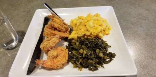 A plate with fried shrimp, macaroni and cheese, and collard greens, served with a knife and fork.