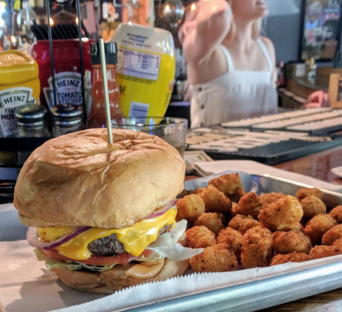 A cheeseburger with lettuce, tomato, and onion on a tray, accompanied by a side of crispy tater tots.