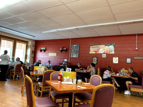 A cozy diner with patrons seated at tables, a server attending to customers, and red walls adorned with decor.