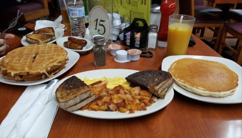 A table with a breakfast spread: waffles, pancakes, scrambled eggs, hash browns, toast, and drinks.