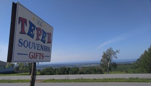 Sign for "The Tepee Souvenirs Gifts" with a scenic view of hills and a clear blue sky in the background.