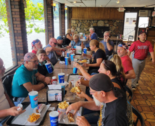 A group of people dining together at a restaurant, enjoying food and drinks by a window with a view of the water.