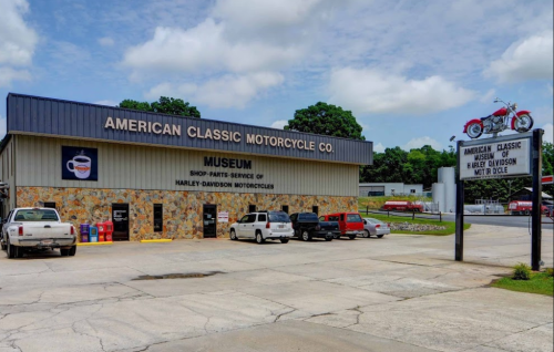Exterior of the American Classic Motorcycle Co. museum, featuring a sign and a motorcycle display on the roof.