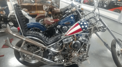 A collection of vintage motorcycles, featuring a chopper with an American flag design and a classic blue bike in the background.