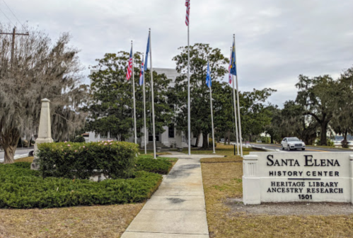 Sign for Santa Elena History Center with flags and greenery in front of a building.