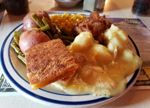 A plate of food featuring fried chicken, green beans, corn, red potatoes, cornbread, and creamy mashed potatoes with gravy.
