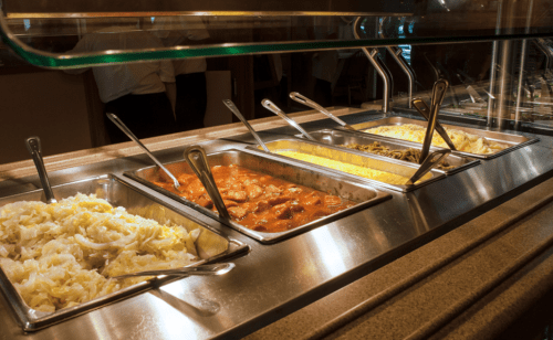 A buffet display with four trays of various dishes, including cabbage, meat stew, pasta, and rice.