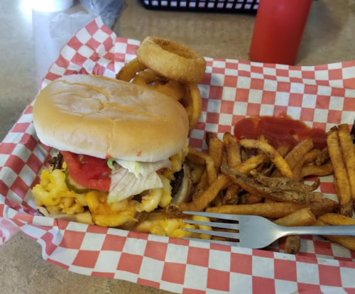 A burger with lettuce, tomato, and cheese, served with fries and onion rings in a red-checkered basket.