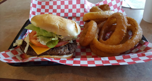 A cheeseburger with lettuce, tomato, and onion rings on a red and white checkered tray.