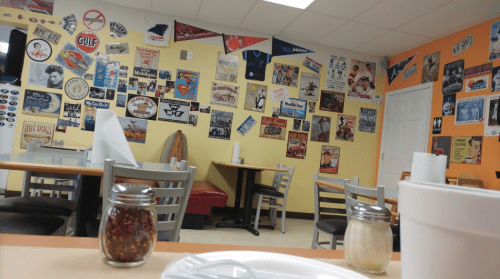 A cozy diner with colorful vintage signs on the walls, empty tables, and condiments on the table.