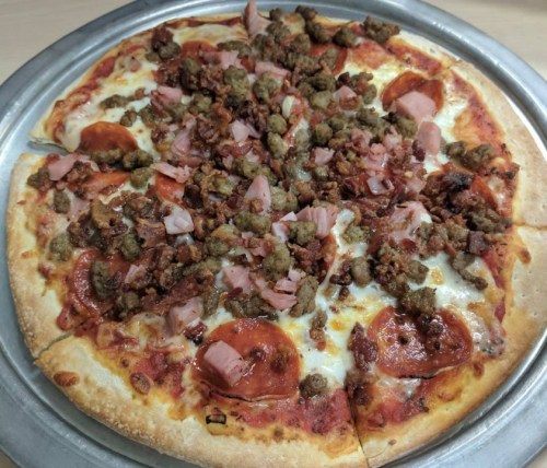 A large pizza topped with pepperoni, ham, sausage, and crispy bacon on a golden crust.